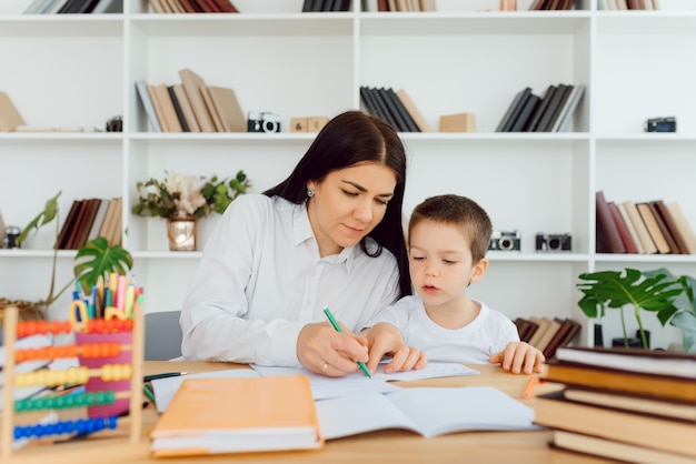 Retrato de niño guapo en el lugar de trabajo con su tutor sentado cerca y diciendo algo