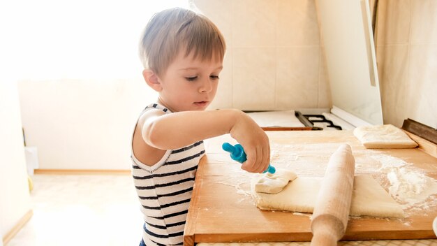 Retrato de niño haciendo masa en encimera de cocina de madera. Niño horneando pasteles o galletas para el desayuno