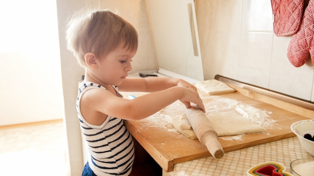 Retrato de niño haciendo masa sobre encimera de cocina de madera