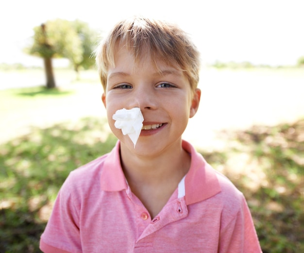 Foto retrato de niño y hemorragia nasal o papel para aventura al aire libre o lesión en accidente o sonrisa niño y rostro feliz con pañuelo para sangre en el patio de recreo del bosque para actividad física, deportes o naturaleza