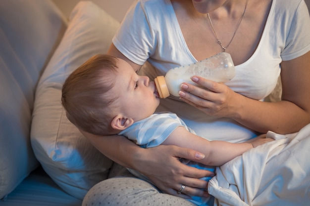 Retrato de niño hermoso bebiendo leche de botella por la noche