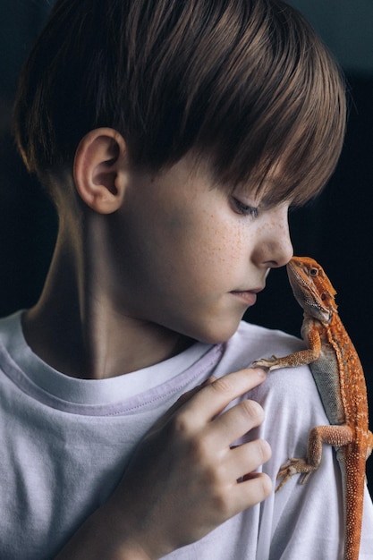 Retrato de niño con iguana agama barbuda roja sobre fondo gris niño pequeño jugando con reptil