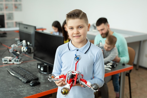 Retrato de un niño inteligente en una clase de robótica en la escuela sosteniendo un robot que ensambló de plástico