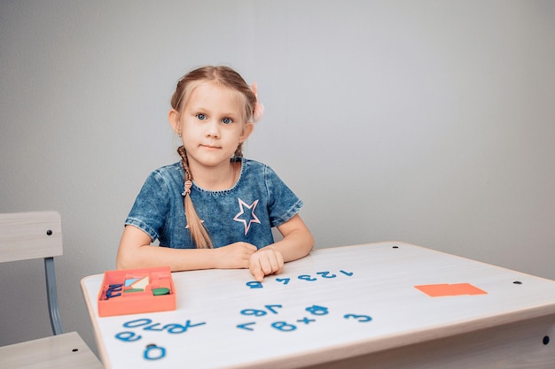 Retrato de un niño inteligente enfocado sentado en una mesa blanca con números en el orden correcto