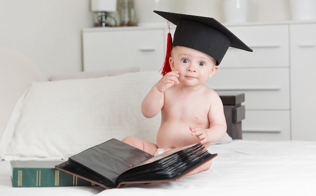 Retrato de niño inteligente en gorro de graduación posando con libros