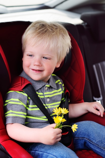 Retrato de un niño joven de un niño con cabello rubio en un asiento de auto para niños.