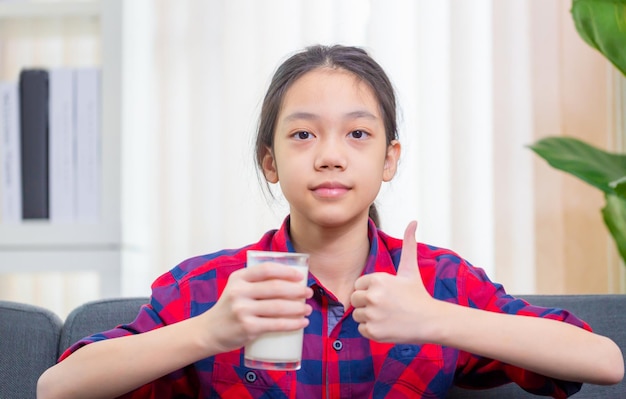 Retrato de niño lindo asiático sosteniendo una taza de leche y mostrando los pulgares hacia arriba Niña feliz bebe leche