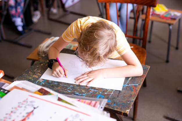 Retrato de niño lindo con bolígrafo y papel en el escritorio en el aula