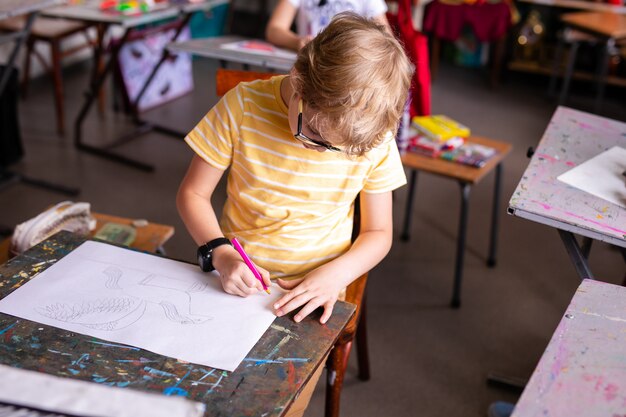 Retrato de niño lindo con bolígrafo y papel en el escritorio en el aula