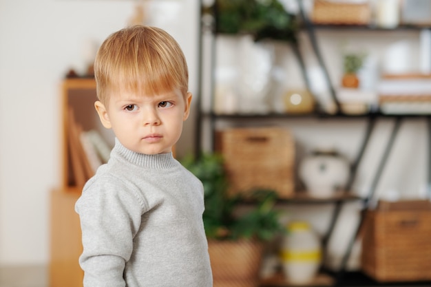 Retrato de niño lindo con cabello rubio de pie en la habitación