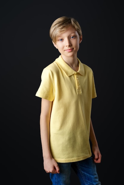 Foto retrato de un niño lindo con una camiseta amarilla sobre un fondo negro posando para la cámara