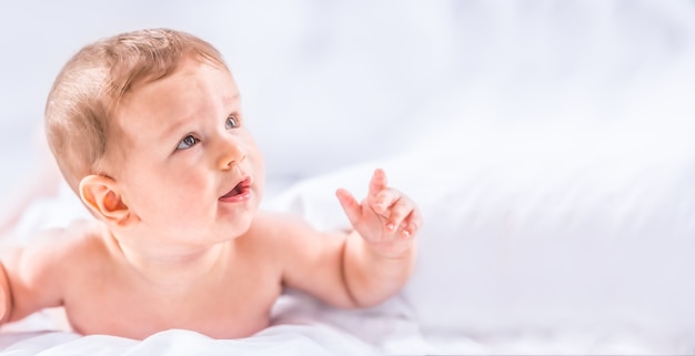 Retrato de niño lindo niño acostado en la cama. Niño recién nacido en el dormitorio. El bebé se acuesta boca abajo y levanta la cabeza.