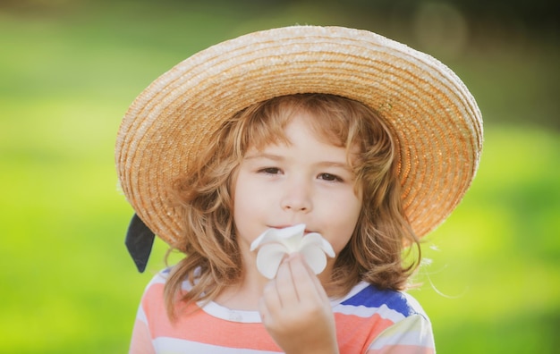 Retrato de un niño lindo niño con sombrero de paja que huele a flor de plumeria Cerrar la cara de los niños caucásicos Primer plano de la cabeza de un niño divertido