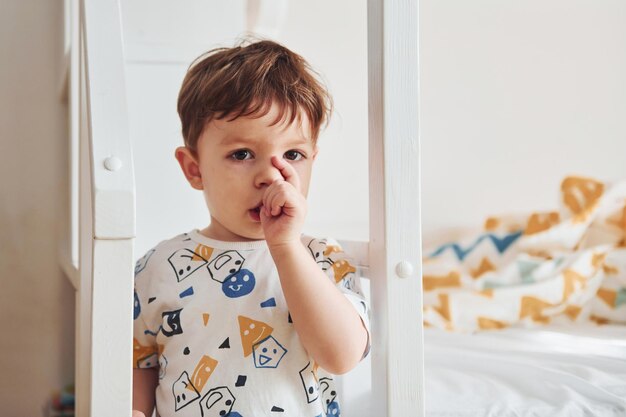 Retrato de un niño lindo que está parado adentro en el dormitorio