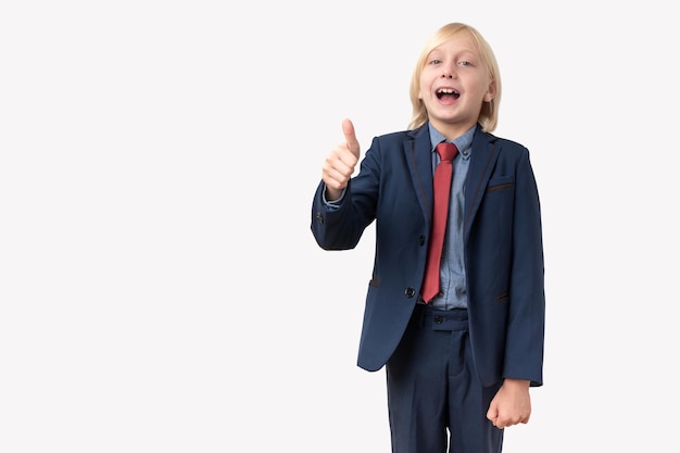 Retrato de un niño lindo en un traje que muestra los pulgares hacia arriba sobre un fondo blanco