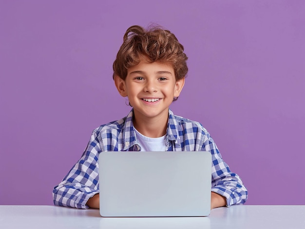 Retrato de un niño lindo usando una computadora portátil mientras está sentado en la mesa contra un fondo púrpura