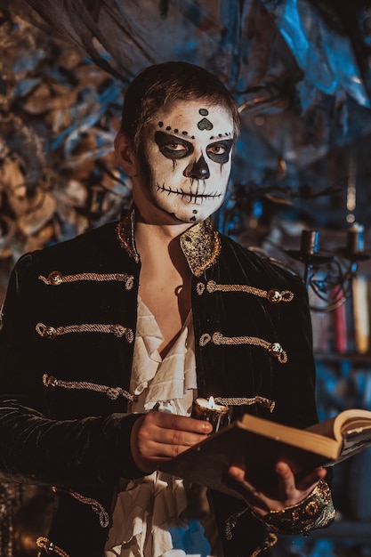 Retrato de un niño en el maquillaje de un loco loco de pie en un interior fabuloso con un libro antiguo y una vela en las manos