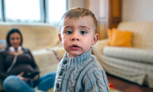 Retrato de niño mirando a la cámara con su madre embarazada sentada en el fondo