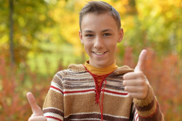 Retrato de niño mostrando los pulgares para arriba en el parque otoñal