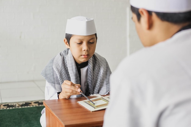Retrato de un niño musulmán religioso aprendiendo a leer el Corán con ropa de estilo árabe en la mezquita