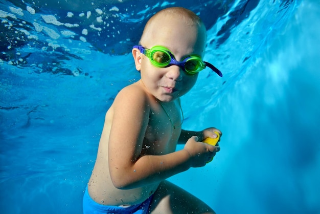 Foto retrato de un niño nadando bajo el agua en una piscina mirando a la cámara y sonriendo