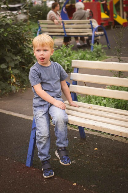 Retrato de un niño un niño rubio de 4 años se sienta en el parque en un banco