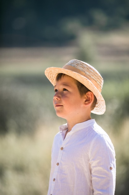 Foto retrato del niño de pelo rubio con sombrero de paja con fondo de vegetación de verano borroso