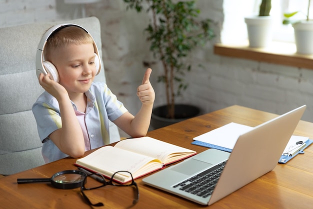 Retrato de niño pequeño con auriculares estudiando en casa mirando en una computadora portátil trabajando con el maestro Educación en línea