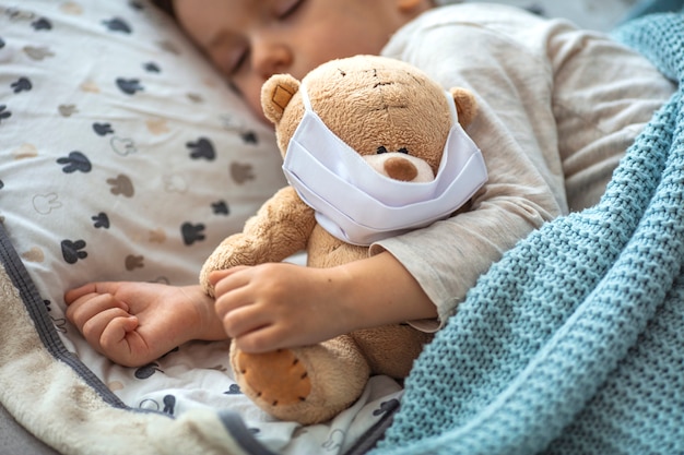 Retrato de un niño pequeño durmiendo y oso de peluche con máscaras de aire. niño en casa en cuarentena durmiendo.