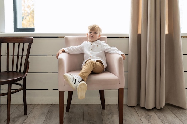 Retrato de un niño pequeño y elegante sentado en una silla con una camisa blanca