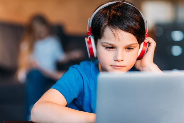 Retrato de niño pequeño enfocado en auriculares usando laptop