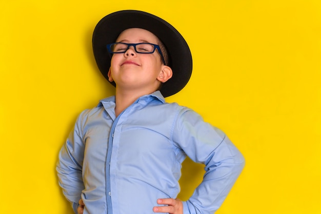 Retrato del niño pequeño hermoso orgulloso en el sombrero y la camisa aislados en amarillo