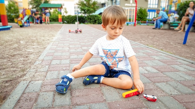 Retrato de niño pequeño jugando con coches de juguete en el patio de recreo