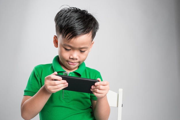 Retrato de un niño pequeño lindo divertido jugando en el teléfono inteligente aislado