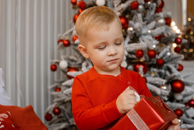 Retrato de un niño pequeño lindo encantador que sostiene la caja de regalo envuelta y que mira atentamente su regalo de Navidad