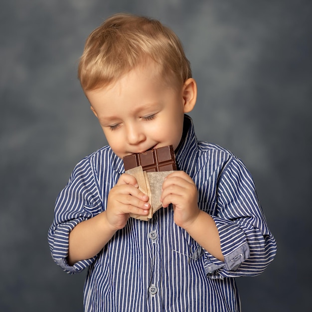 Retrato de niño pequeño niño comiendo chocolate sobre fondo gris concepto de infancia feliz goloso