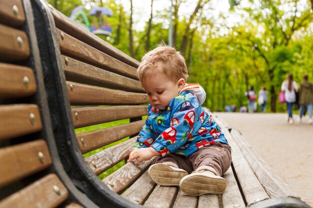 Retrato de un niño pequeño en el parque en un banco atrapando pompas de jabón