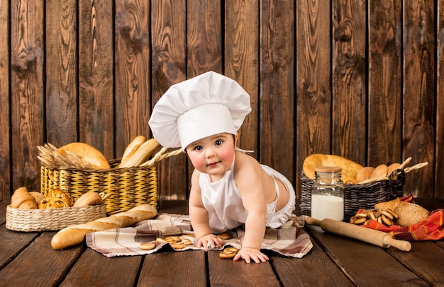 Retrato de un niño pequeño en ropa de chef entre productos de panadería sobre un fondo de madera