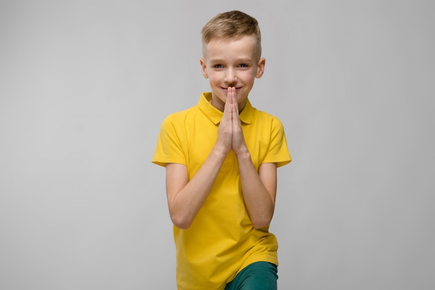 Retrato de niño pequeño rubio caucásico lindo en camiseta amarilla esperando en gris