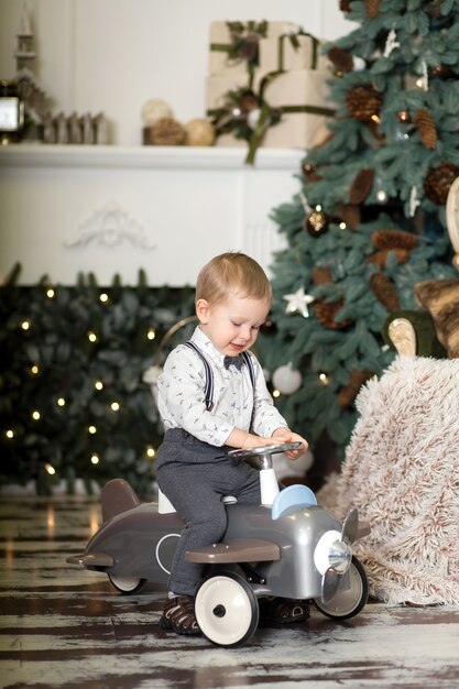 Retrato de un niño pequeño sentado en un avión de juguete vintage cerca de un árbol de Navidad