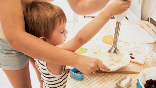 Retrato de niño pequeño sonriente feliz con madre joven para hornear y cocinar en la cocina. Padres enseñando y educando al niño en casa