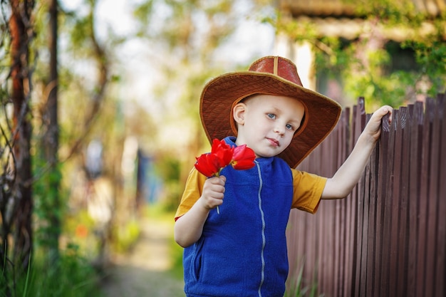 Retrato de un niño de pie en un gran sombrero con un ramo de tulipanes en la valla de madera en el campo