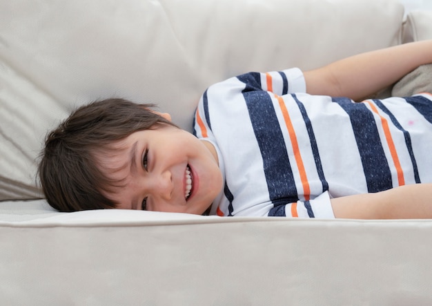 Retrato de niño positivo acostado en el sofá mirando a cámara con cara sonriente