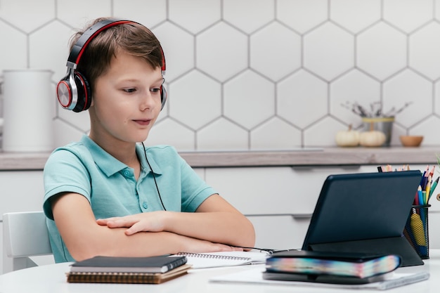 Retrato de un niño preadolescente sentado cerca de cuadernos mirando la pantalla de la tableta con una lección en línea en casa