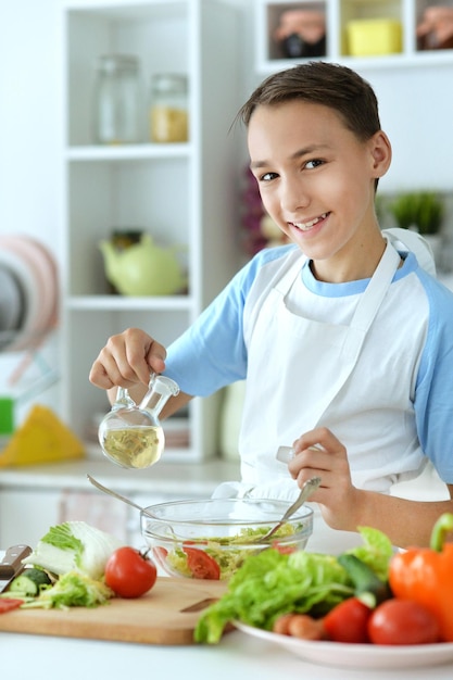 Retrato de niño preparando ensalada en la mesa de la cocina en casa