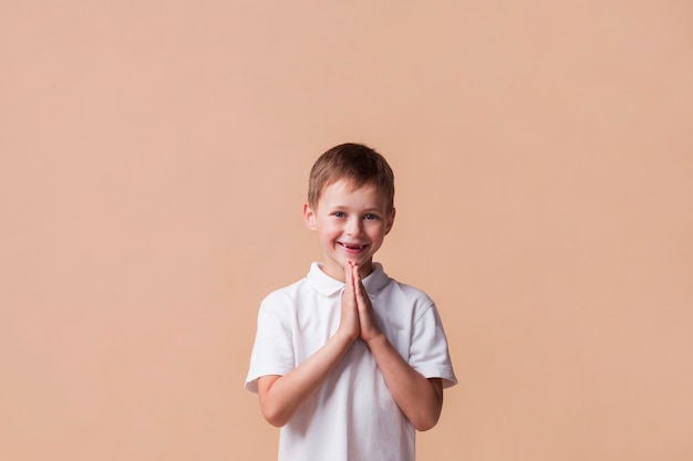 Foto retrato de niño rezando con una sonrisa en su rostro sobre fondo beige