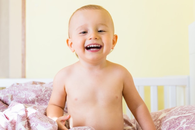 Retrato de un niño riendo sentado en la cama en la habitación