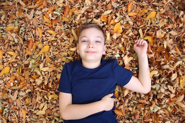 Foto retrato de un niño rubio de 9 años en un parque de otoño en hojas caídas de naranja