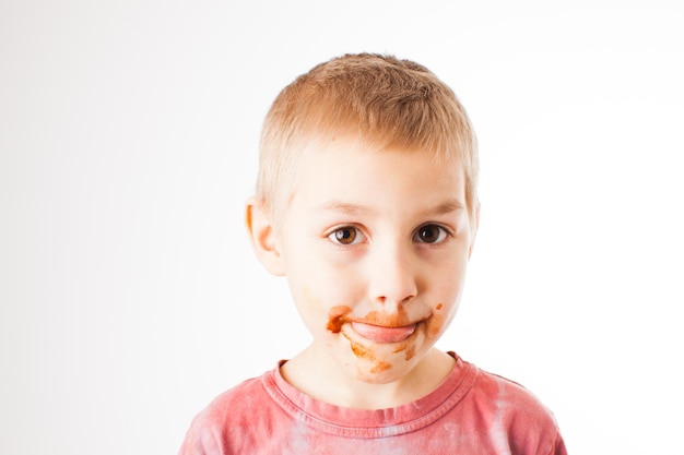 Retrato de niño rubio con chocolate en la cara aislado en blanco. Chico después de probar chocolate