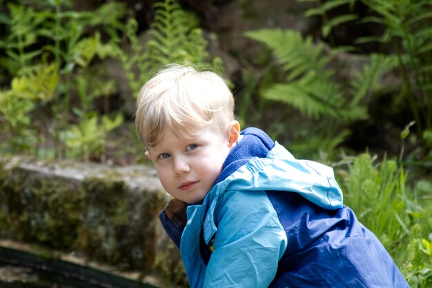 Foto retrato de un niño rubio contra un fondo de follaje verde en el espacio de copia del parque